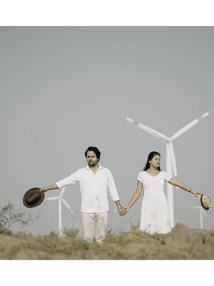 A wide, cinematic shot of a couple against a backdrop of windmills, creating a sense of adventure for their pre-wedding album.