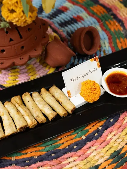 Golden and crispy Thai Cigar Rolls served on a black platter with a sweet chili dipping sauce. These flavour-packed rolls are a perfect pass-around snack for any gathering.