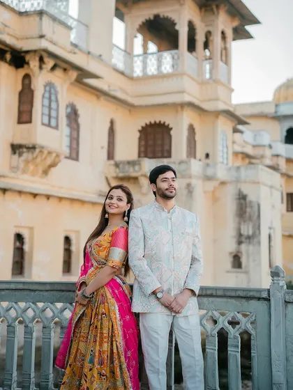 A classic portrait of a couple in vibrant traditional attire in front of a palace in Udaipur. The colorful outfits stand out beautifully against the heritage architecture.