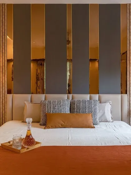 A luxurious bedroom featuring a dramatic back wall with alternating panels of grey, rose-gold mirror, and fluted wood. The design is opulent, modern, and rich in texture.