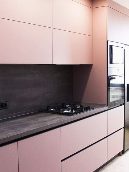 Thinking pink? This kitchen showcases how a soft pink can create a chic and modern look. The matte pink handle-less cabinets are paired with a dark grey countertop and backsplash for a sophisticated contrast.