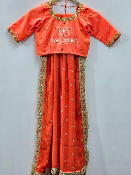 A complete half-saree set in a vibrant orange. The set includes a blouse, a skirt, and a dupatta with a heavy embroidered border.