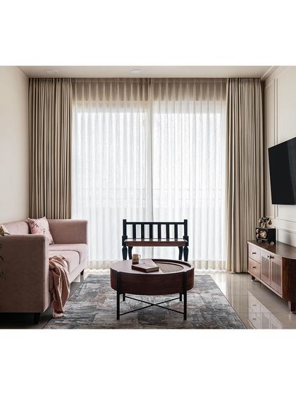 Designed for simplicity, this living area features a blush pink sofa that adds a modern touch against the neutral walls. The TV unit is designed to conceal gadgets, maintaining a timeless and uncluttered look.