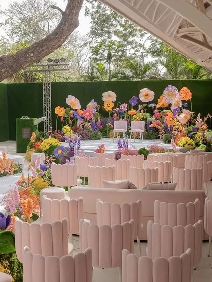 A wide view of the ceremony seating for the "Bloom" wedding, with rows of chic pink shell-backed chairs creating a stunning visual against the vibrant floral aisle.