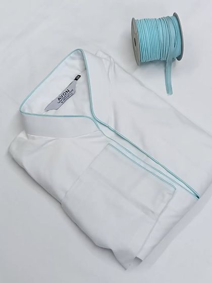 A folded white saya kurta with light blue piping and its matching thread spool. This shows how I carefully match the colors for a perfect finish.
