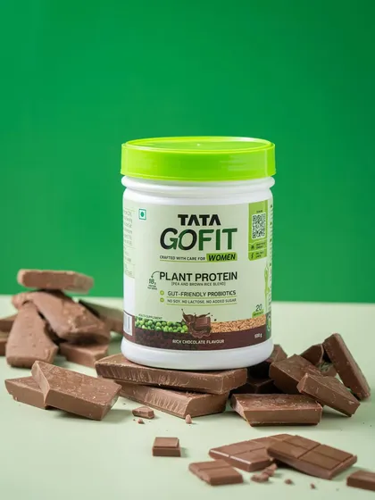 A bold product shot with the Tata GoFit tub sitting on a pile of chocolate, visually reinforcing the rich chocolate flavor of the plant protein.
