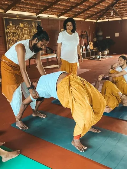I assist a student in a supported wheel pose, helping them to open their chest and shoulders safely. This kind of partner work and trust is integral to the learning process.