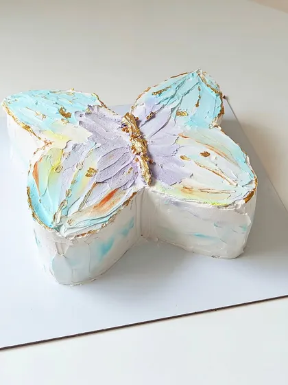 A unique butterfly-shaped cake with a dreamy, watercolor-like buttercream finish in pastel colors. Gold leaf accents give this artistic cake a touch of shimmer.