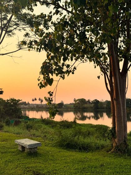 A quiet stone bench by the river offers a perfect spot for contemplation as the sun sets. The warm colors reflecting on the water create a peaceful mood, ideal for a walking meditation or simply being present.