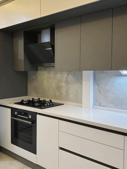 A two-tone kitchen design with matte grey upper cabinets and white lower cabinets. The built-in oven and hob are strategically placed for ergonomic use, and the marble-patterned backsplash adds a touch of luxury.