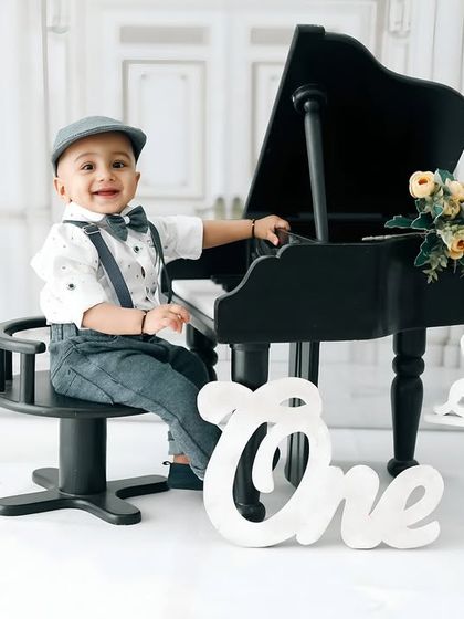 A joyful smile from the birthday boy at his miniature piano. This classic, clean setup puts all the focus on his happy expression and adorable outfit.