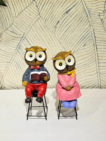 A wise owl couple, dressed up and sitting on stools, makes for a whimsical and charming decor piece.
