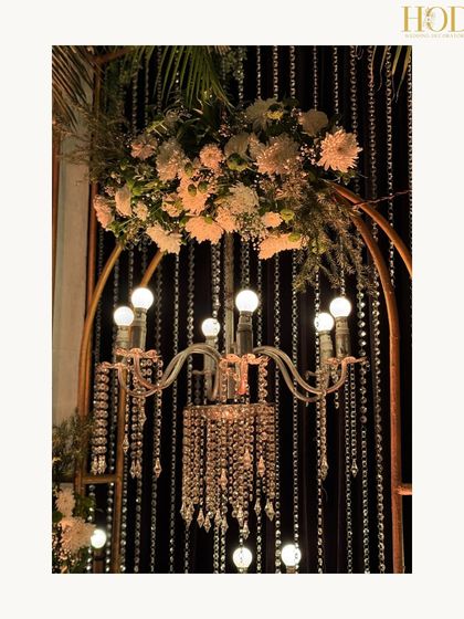 A close-up of a chandelier nestled within a floral arrangement on a golden arch, a beautiful and intricate artistic detail.