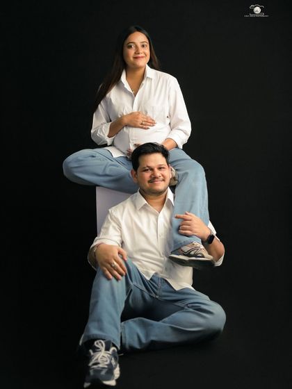 A playful and unique pose showing the couple's fun-loving personality. The mother-to-be sits on her partner's shoulders, both smiling at the camera in matching casual outfits.