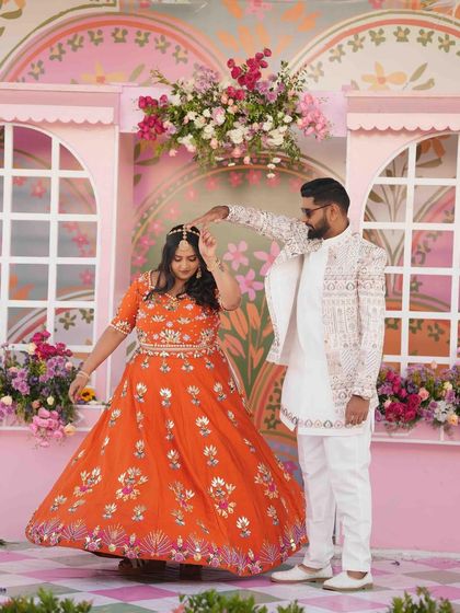 A happy couple lost in their dance. The vibrant orange of the bride's lehenga and the colorful decor come together to create a picture of pure celebration.