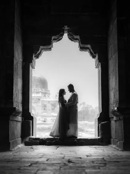 A timeless black and white silhouette, framed by the arches of a historic monument. This artistic style focuses on form and emotion, creating a powerful and classic pre-wedding portrait.