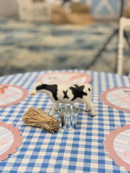 A close-up of the farm-themed centerpiece, with a toy cow, mini hay bale, and personalized placemat on a classic gingham tablecloth.