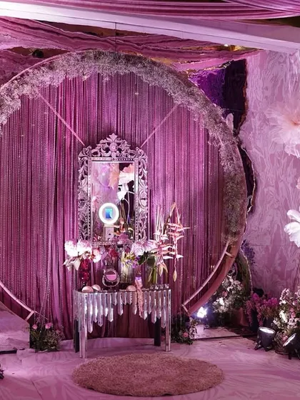 A full view of the whimsical circular photo booth, showing the oversized floating flowers and the elegant mirrored console table at its center.