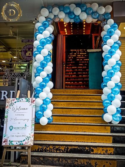 We created this welcoming entrance for a cafe's anniversary celebration. A classic balloon arch in blue and white guides guests up the stairs, with a custom welcome sign on an easel to greet them.