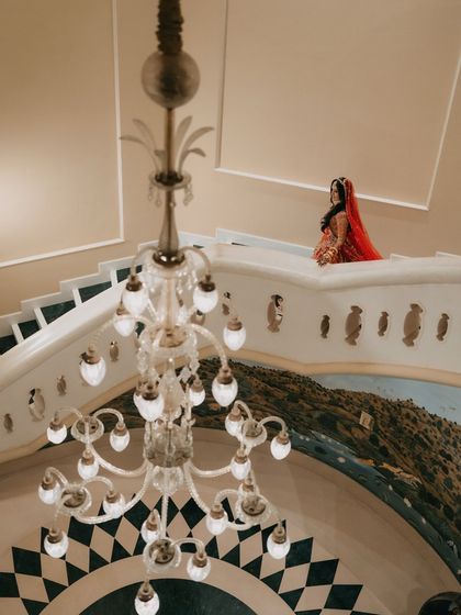 An architectural shot of the bride on a palace balcony, with a grand chandelier in the foreground. This image plays with scale and perspective to create a dramatic and artistic portrait.
