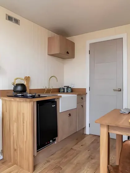 This kitchenette in a container home is both stylish and functional, with a farmhouse sink, wooden countertops, and open shelving. It proves that you don't need a lot of space to have a beautiful kitchen.