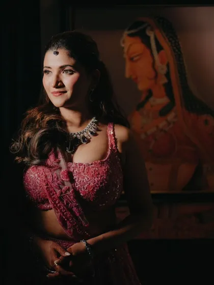 A beautifully lit portrait of the bride at her Sangeet, her expression serene as she stands beside a classic painting.