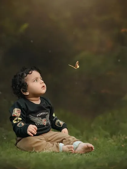 A simple, beautiful portrait of a little boy watching a butterfly. The dark, natural background makes him the clear focus of this enchanting photo.
