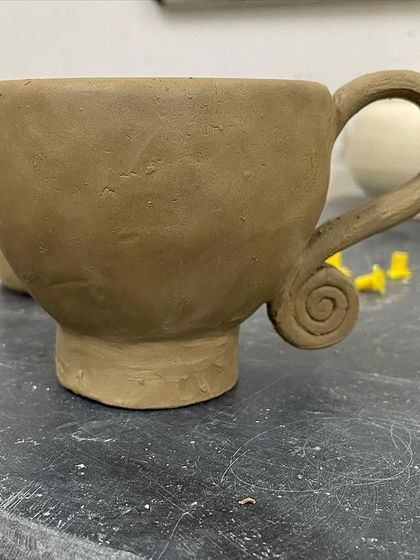 A hand-built cup with a charming, curled handle, waiting to be fired and glazed.