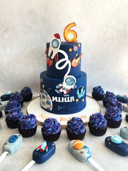 An out-of-this-world dessert table for Mihir's 5th birthday. The space-themed cake is orbited by matching cupcakes and cakesicles shaped like planets and rockets.