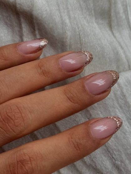 A beautiful rose gold glitter French tip on natural, oval-shaped nails.