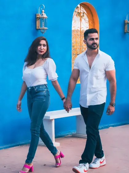 A vibrant and stylish pre-wedding photo of a couple walking hand-in-hand against a bright blue wall.