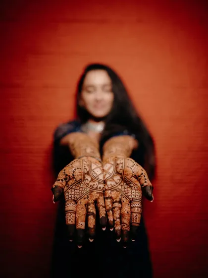 An artistic shot with the bride out of focus in the background, drawing all attention to the stunningly detailed mehendi in the foreground.