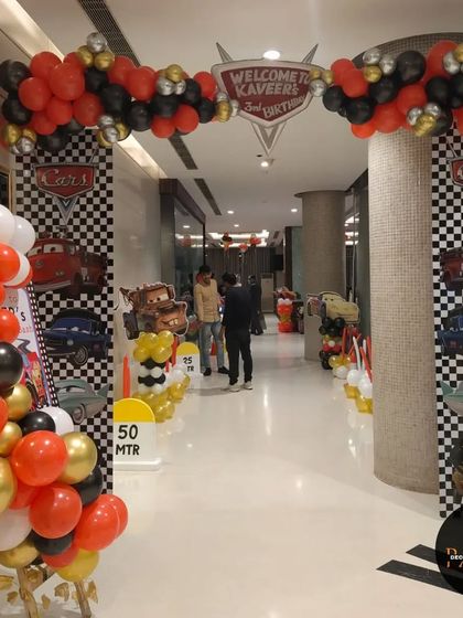 The grand entrance walkway for a 'Cars' party, lined with character banners and balloon decorations.