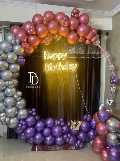 A detailed look at the circular balloon arch for a birthday celebration. The arrangement features metallic purple, silver, and rose gold balloons with small butterfly accents for a touch of whimsy.