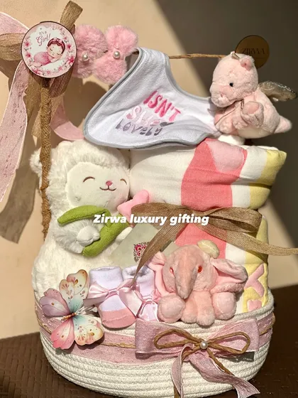 Isn't she lovely? This beautiful hamper for a baby girl is stacked with essentials, including a soft blanket, plush toys, and tiny shoes, all in a sweet pink and white color scheme.
