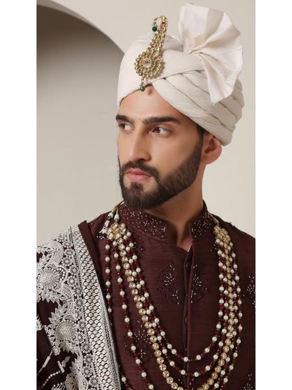 A close-up of the 'Coco Royal' sherwani, focusing on the rich chocolate brown fabric and the elegant ivory pearl necklace. This is a unique and sophisticated color combination for a groom.