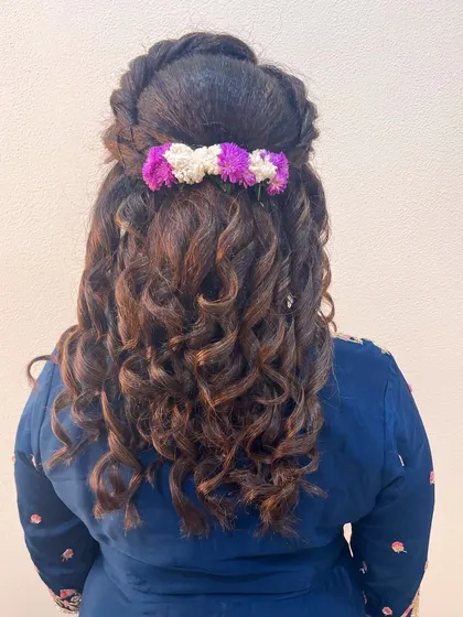 A beautiful half-up hairstyle with voluminous curls, decorated with a gajra of purple and white flowers.
