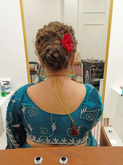 A textured and braided messy bun, accented with a single red flower for a touch of color. This style offers a modern twist on the classic bridal updo, perfect for a sangeet or wedding ceremony.