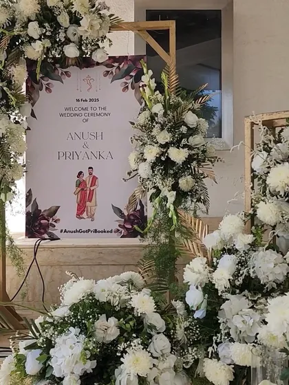 A personalized welcome sign for Anush and Priyanka's wedding, surrounded by a lavish display of white chrysanthemums and roses.