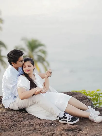 A serene moment of a couple relaxing on a cliffside overlooking the ocean and palm trees. This combines the beauty of a coastal view with a natural, rocky landscape.