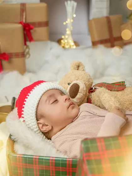 A sleeping newborn in a Santa hat, cozy in a gift box next to a teddy bear. This shot is pure holiday magic, perfect for a birth announcement or Christmas card.