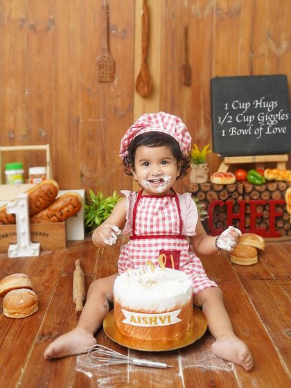 A very proud little chef with her first birthday cake. The chalkboard in the background with a "recipe" for love adds a personal and charming touch to this creative photoshoot.