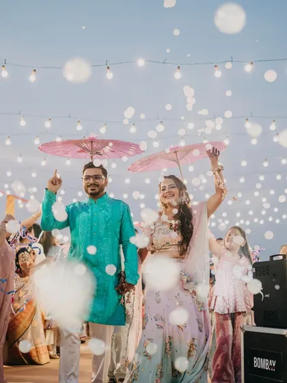 A grand entrance for a Haldi carnival. The couple makes their way in under a shower of bubbles and colorful umbrellas held by their friends, creating a fun and whimsical atmosphere.