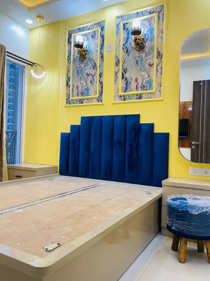 A master bedroom in progress, featuring a bold blue velvet headboard, a matching dressing table, and a vibrant yellow accent wall.