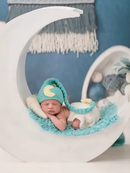 A sweet newborn sleeps peacefully inside a large, crescent moon prop, creating a whimsical and dreamy portrait perfect for a nursery.