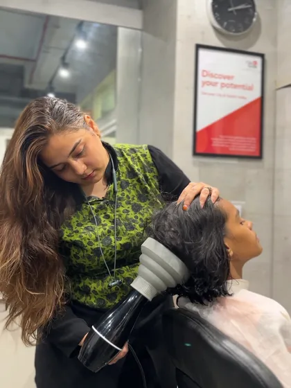 Learning the art of the perfect blow-dry. A student uses a diffuser to style hair, a key finishing skill for any stylist.