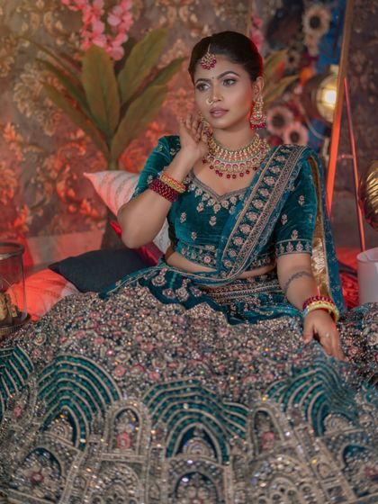 A regal and luxurious look featuring a heavy velvet lehenga. The makeup is rich and opulent, with deep jewel tones on the eyes and lips.