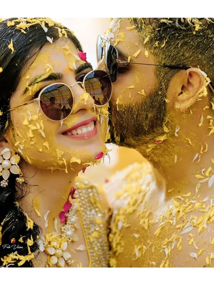 A sweet, intimate moment amidst the Haldi chaos. The groom gives the bride a gentle kiss on the cheek, a beautiful contrast to the high energy celebration.