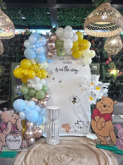 This is our 'A Little Hunny is on the Way' baby shower theme, inspired by Winnie the Pooh. The setup features a custom arched backdrop, character standees of Pooh and Piglet, and a unique balloon arch with a mix of pastel and honey-colored balloons to create a warm, gentle atmosphere.