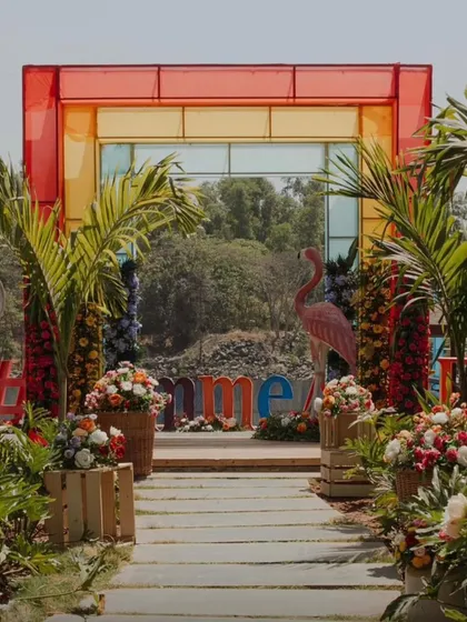 The grand, colorful entrance to a carnival-themed event, with a multi-colored frame, palm trees, and floral arrangements.